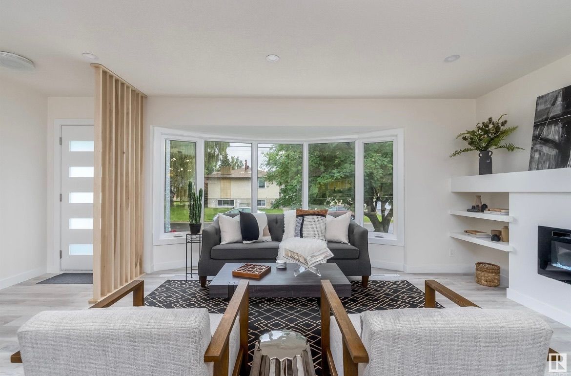 Bright living room with white sofas, large bay window, fireplace, and garden view