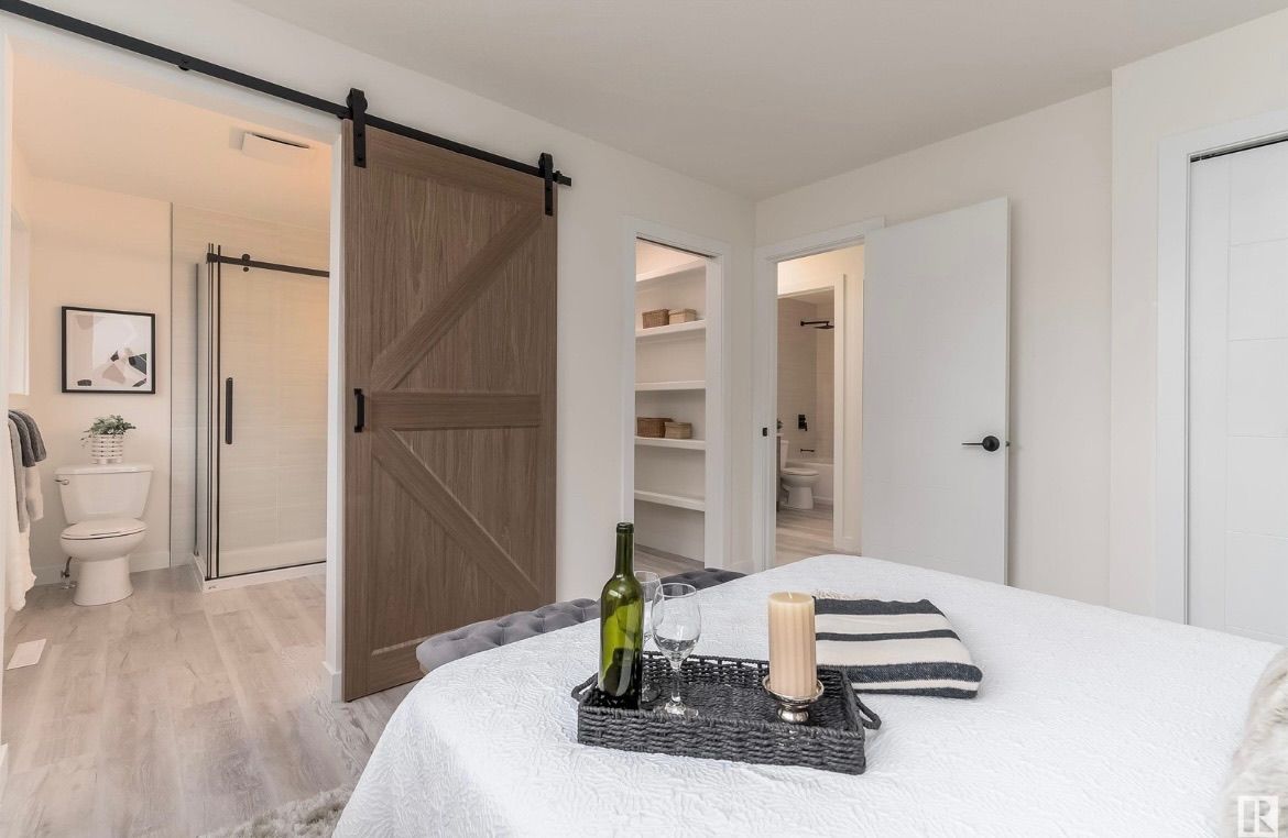Bright bedroom with barn door, open bathroom, and a neatly made bed with tray centerpiece.