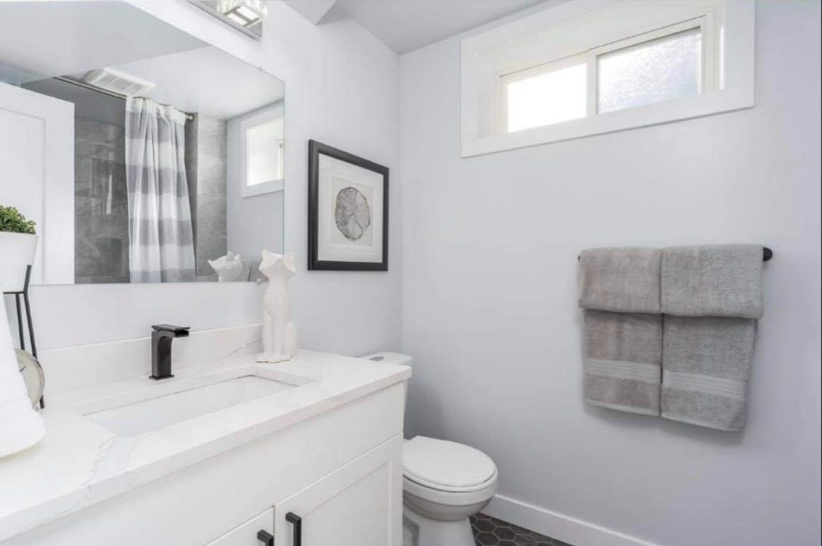 Bright white bathroom with vanity, toilet, tub, window, and gray towels on the wall.