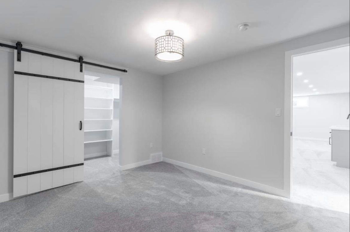 Empty carpeted bedroom with gray walls, a sliding closet door, and bright doorway to an adjoining room