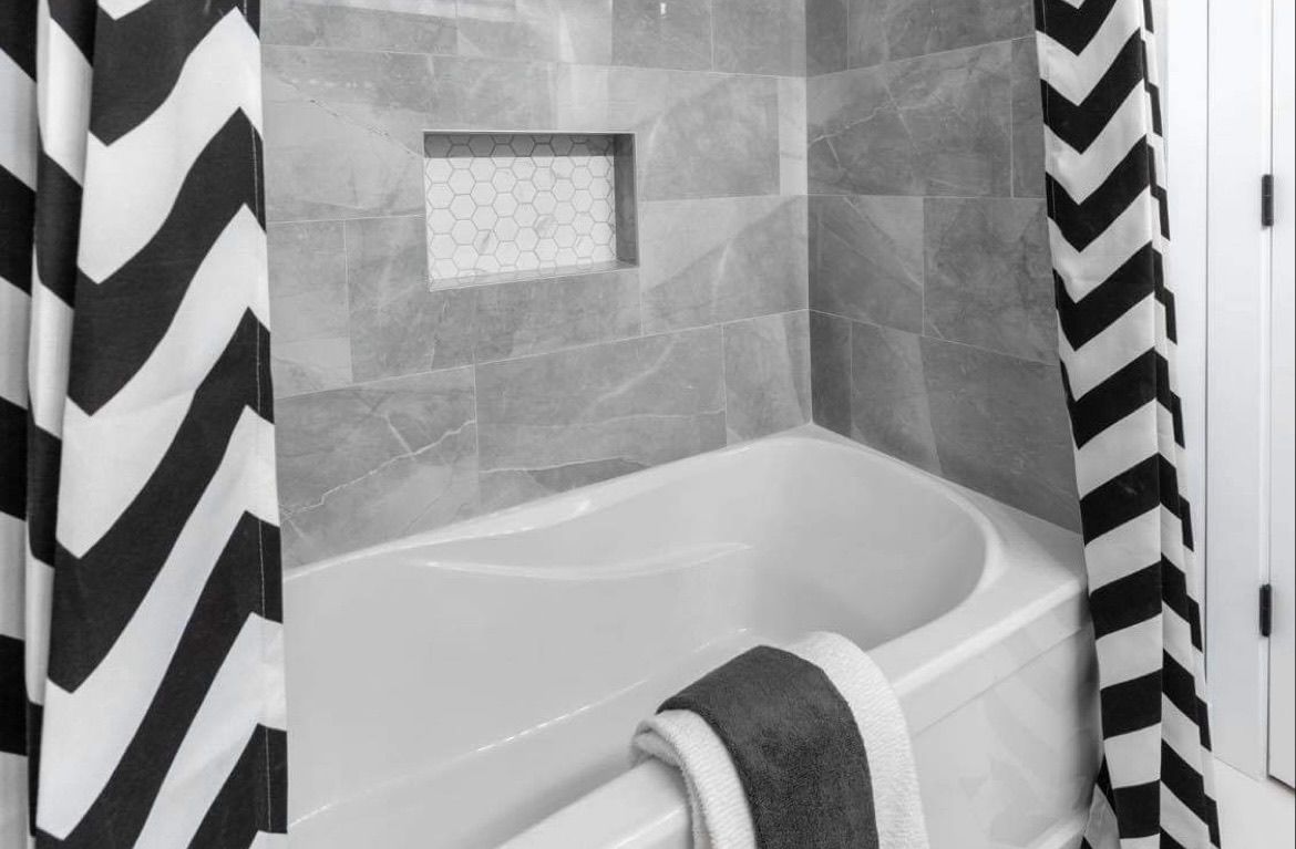 Bathtub in tiled bathroom with black-and-white chevron shower curtains and a towel hanging over the tub.