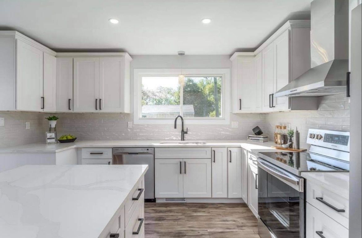 Bright modern kitchen with white cabinets, marble island, stainless steel appliances, and a window above the sink