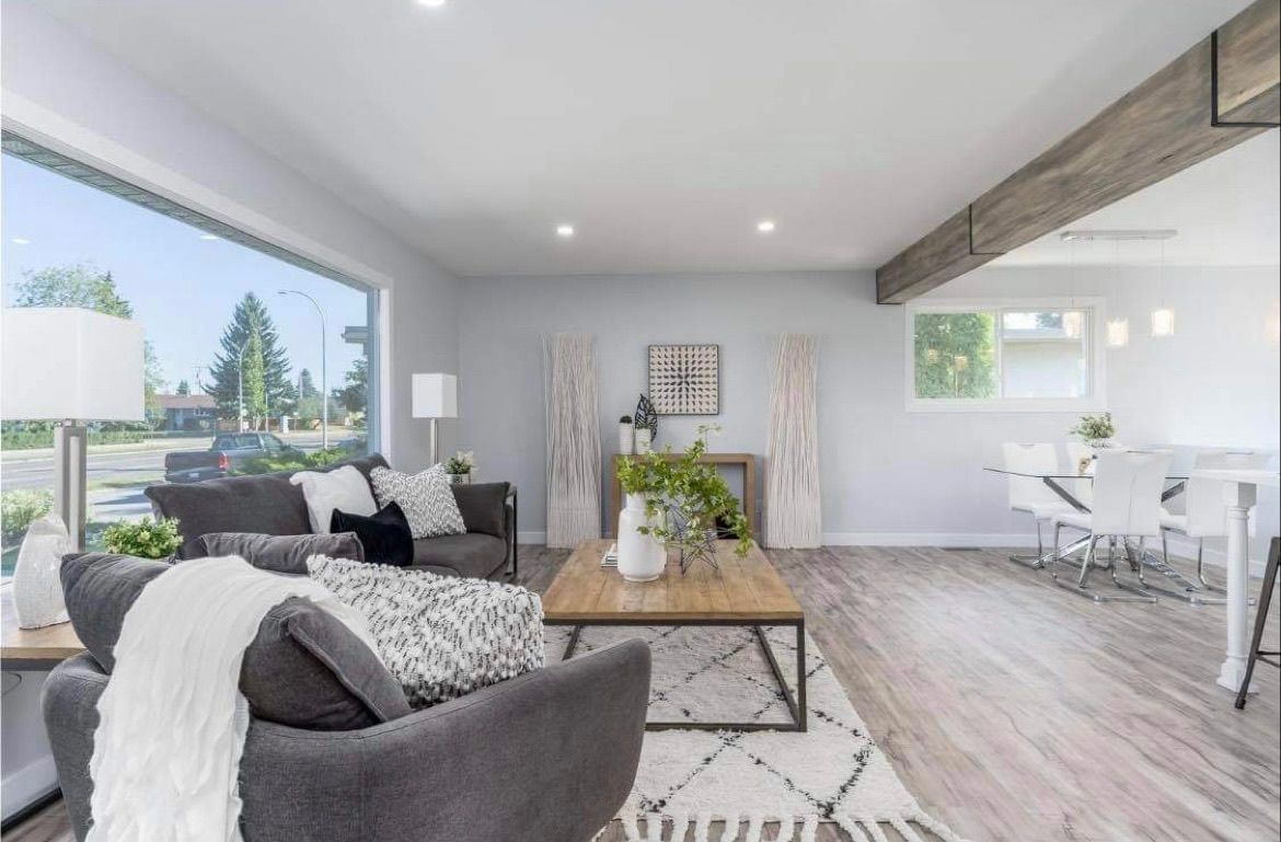 Bright open living room with gray sofa, wooden coffee table, large windows, and dining area beyond