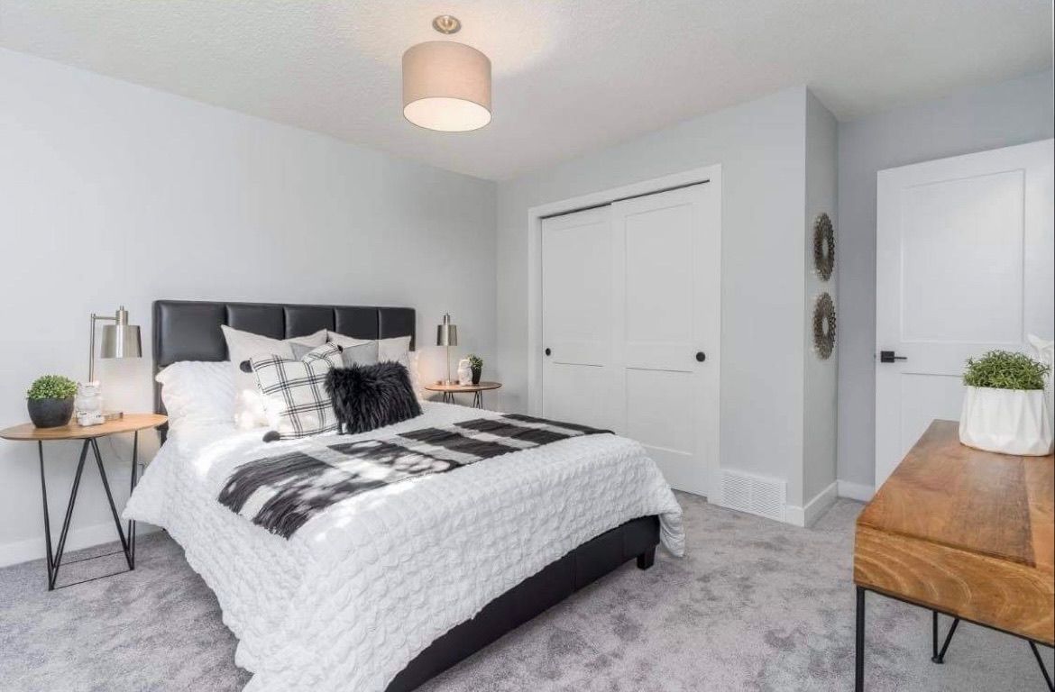 Bright bedroom with a bed, gray carpet, white walls, and wood accents.