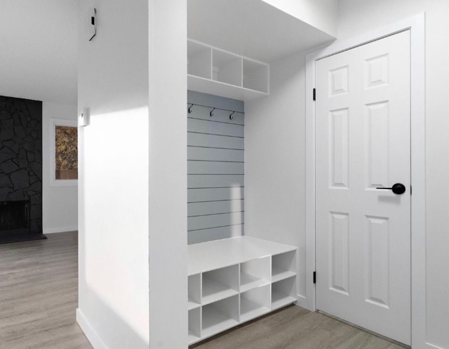 White entryway with built-in bench, cubbies, hooks, and a closed door in a modern home