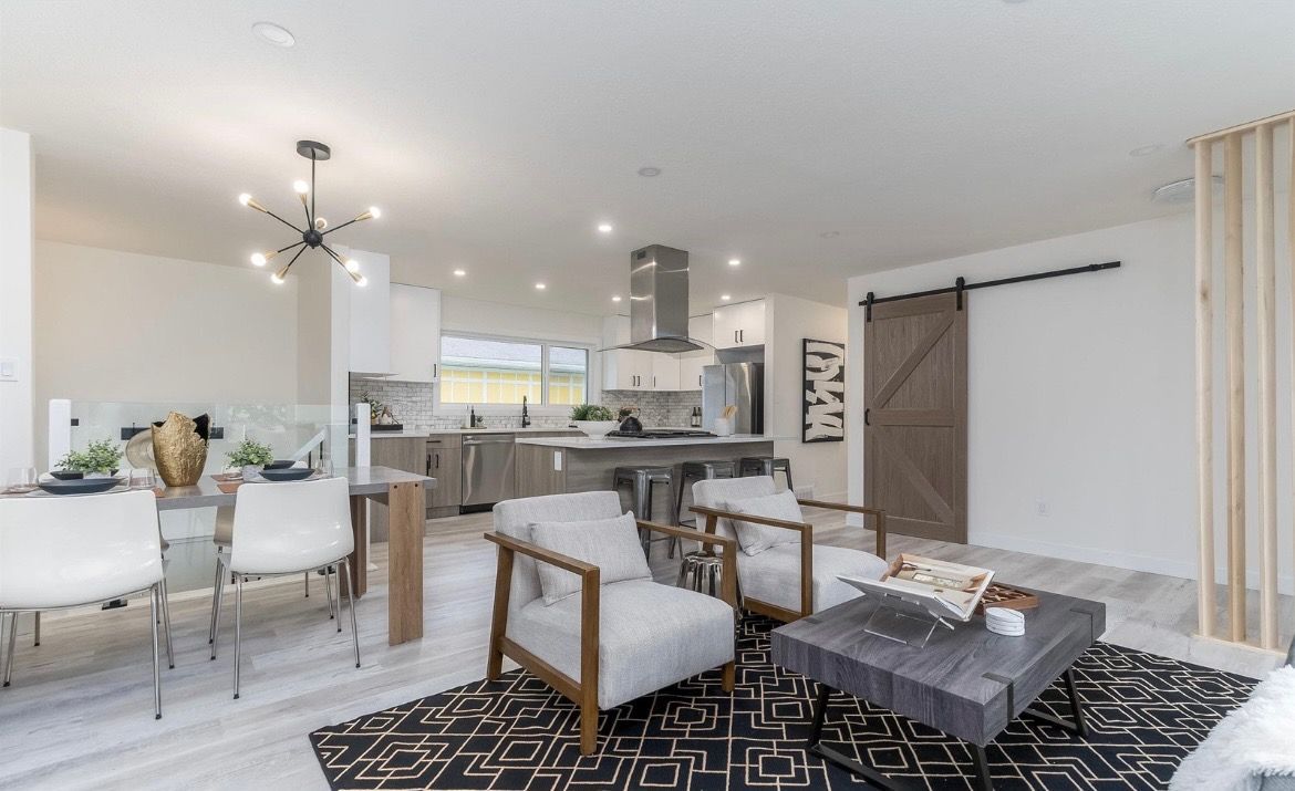 Bright open-plan living room and kitchen with white furniture, black rug, and sliding barn door