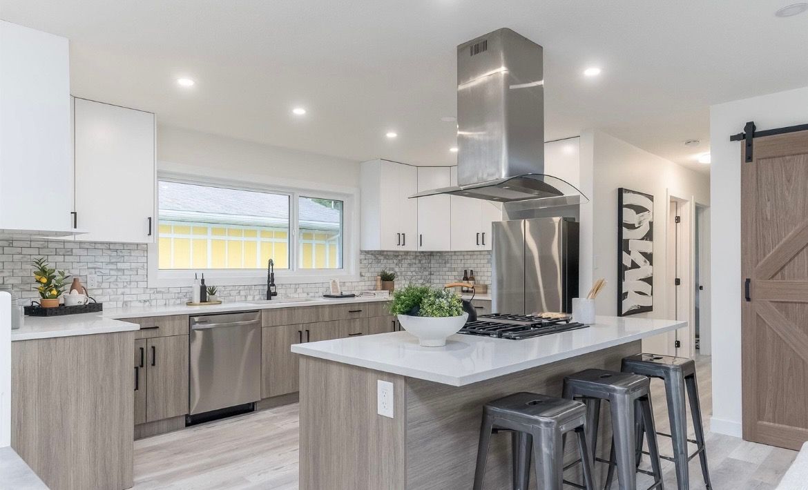Bright modern kitchen with white cabinets, gray island, stainless steel hood, and two stools