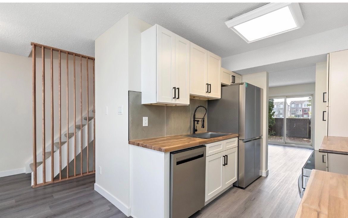 Small modern kitchen with white cabinets, stainless appliances, and gray flooring beside a staircase.