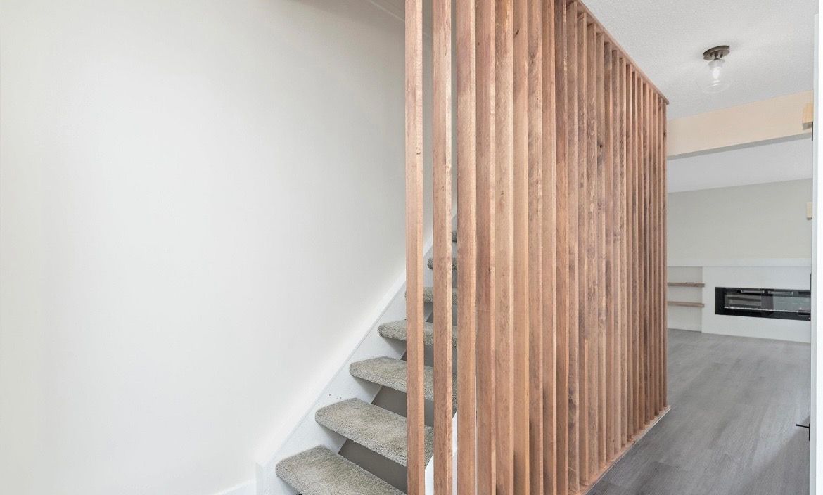 Interior staircase with gray carpet behind a vertical wooden slat partition in a bright modern room
