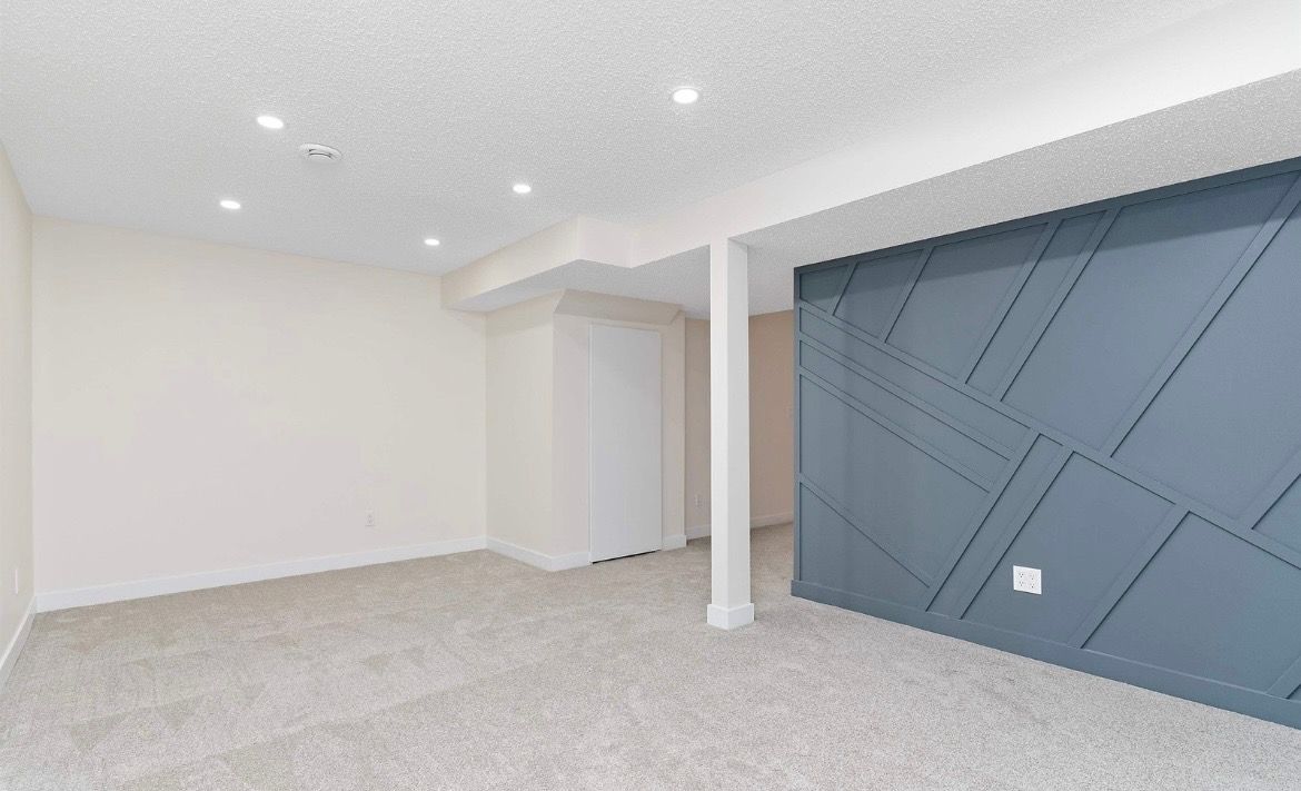 Empty modern room with gray carpet, white walls, a blue accent wall, and recessed ceiling lights