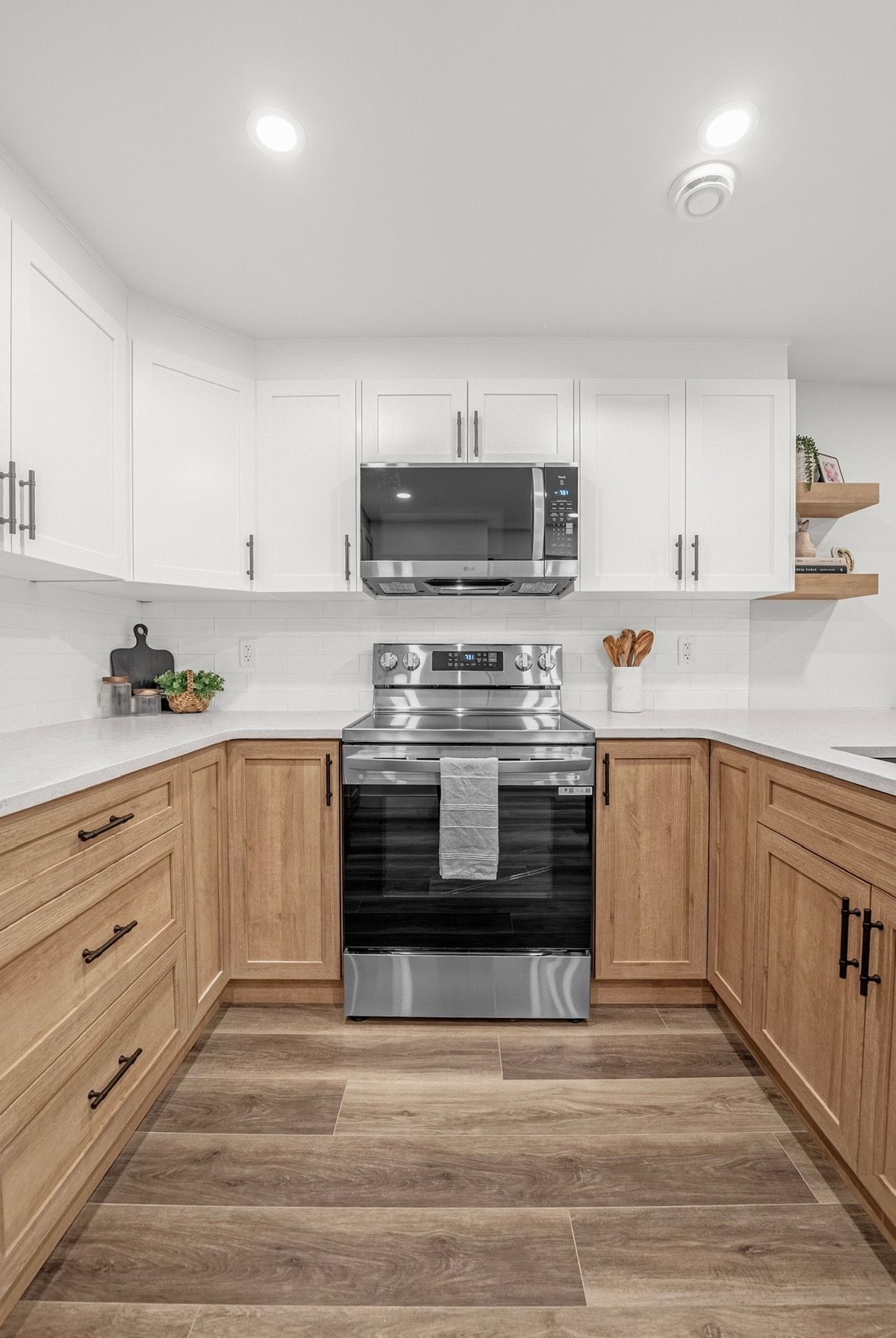 Modern kitchen with white cabinets, wood lower cabinets, stainless steel stove, microwave, and wood-look floor.