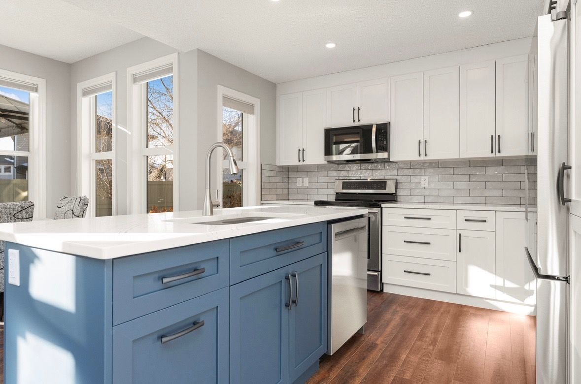 Bright modern kitchen with blue island, white cabinets, stainless appliances, and wood flooring