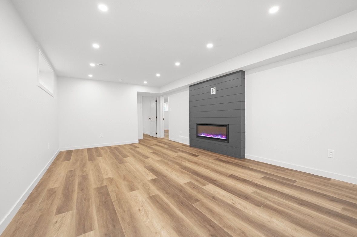Empty modern living room with white walls, wood floors, recessed lights, and a gray fireplace
