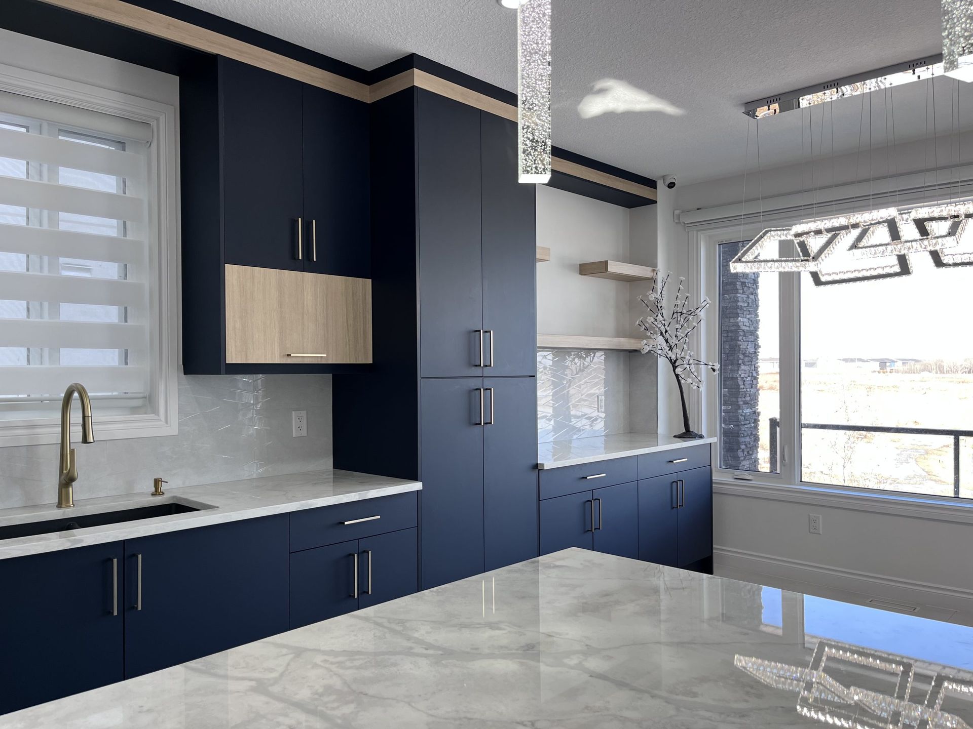 Modern kitchen with dark navy cabinets, white countertops, and a large window overlooking bright light.