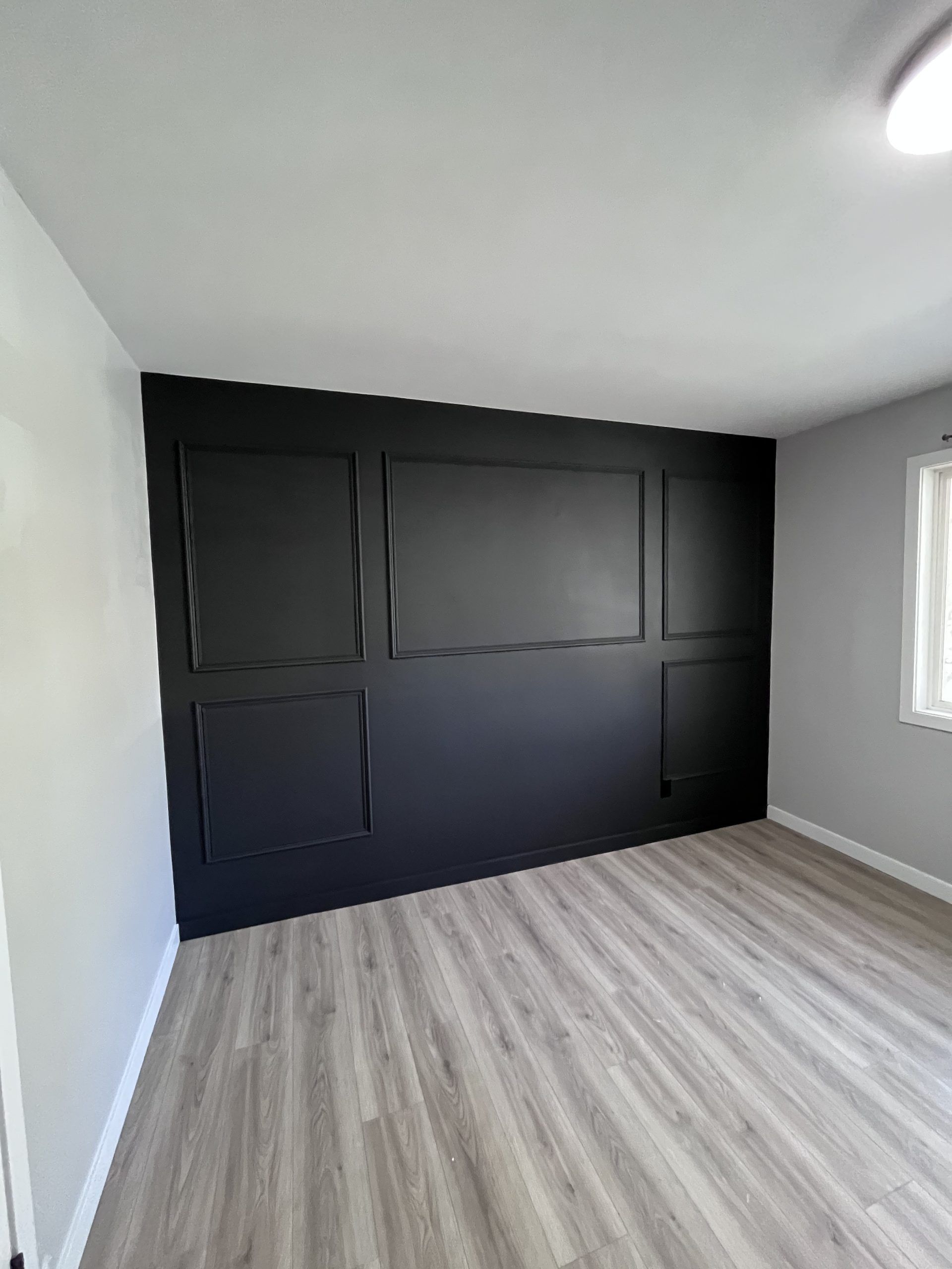 Empty modern bedroom with dark accent wall, light wood floor, gray walls, and a small window