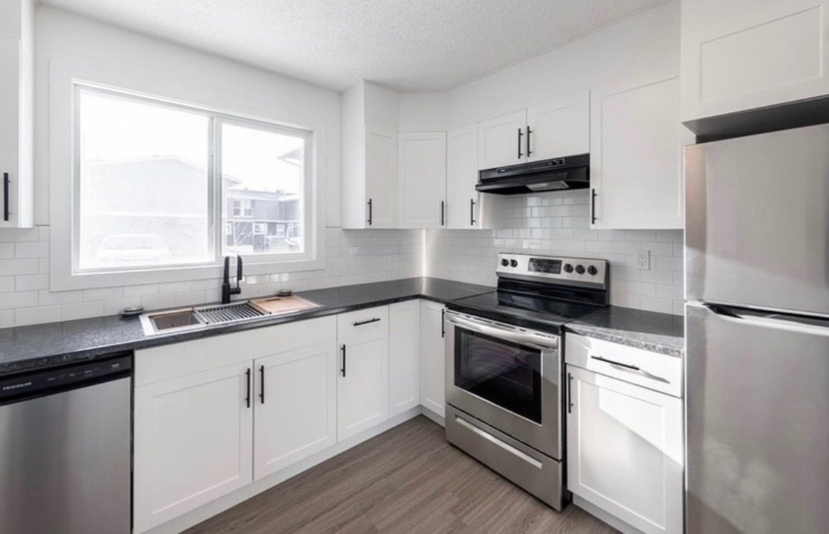 Bright modern kitchen with white cabinets, black countertops, stainless steel appliances, and a window over the sink