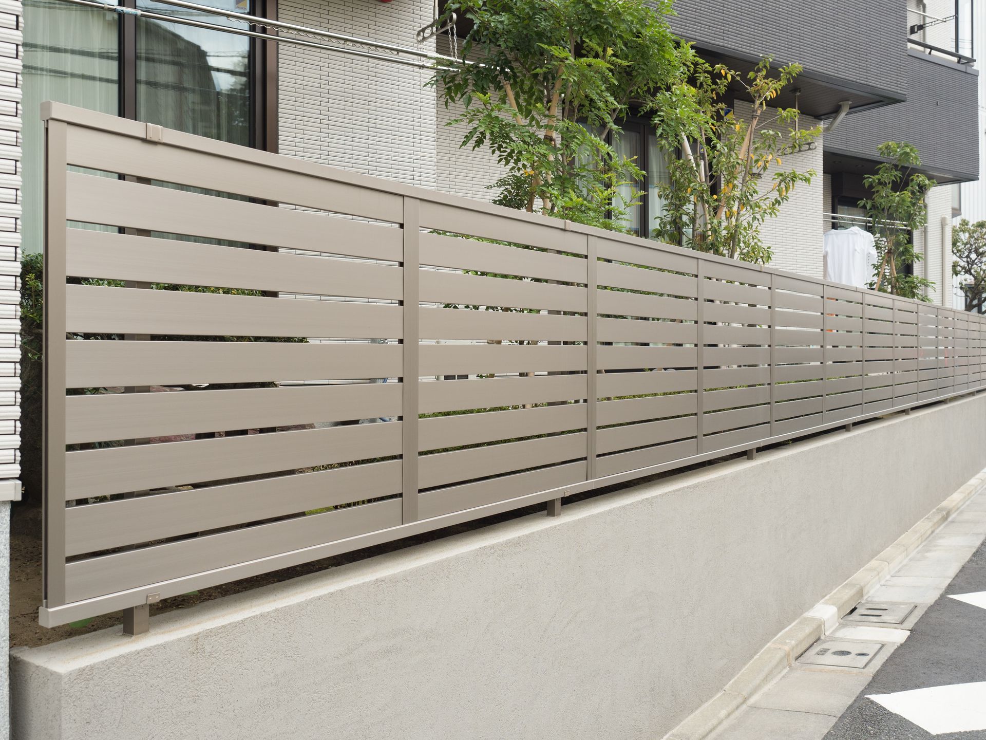 Beige slatted fence along a sloped concrete wall beside a sidewalk and apartment building