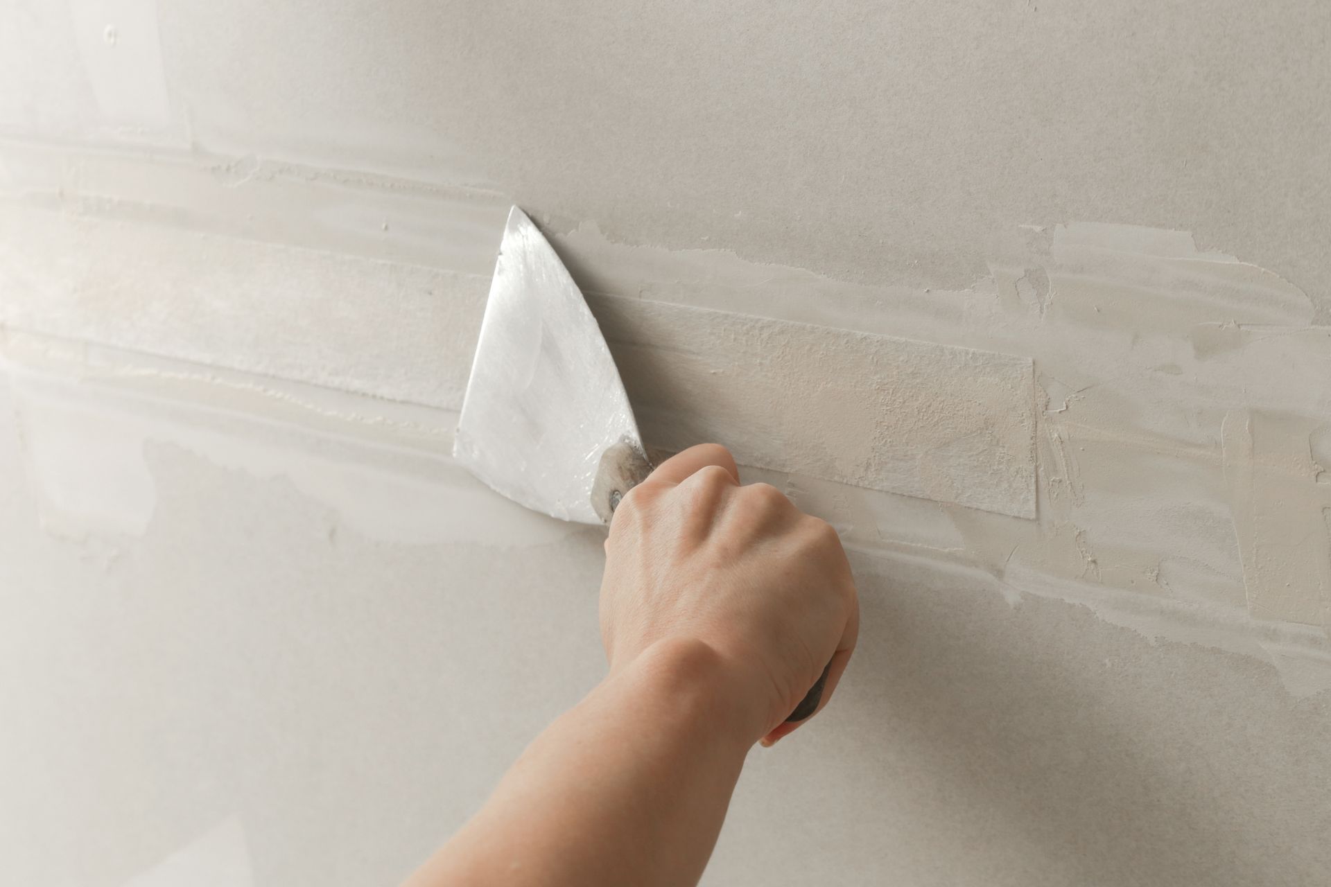 Hand using a putty knife to smooth white drywall compound on a wall