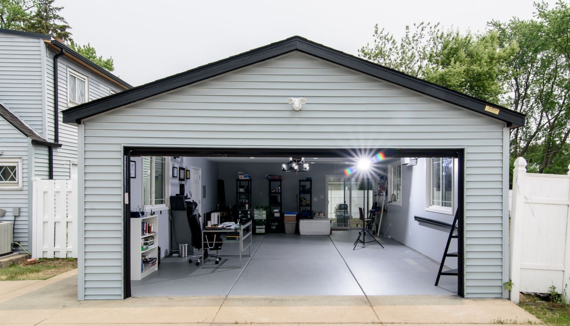 Open garage with a light gray facade, showing a home workshop with tools, benches, and equipment inside