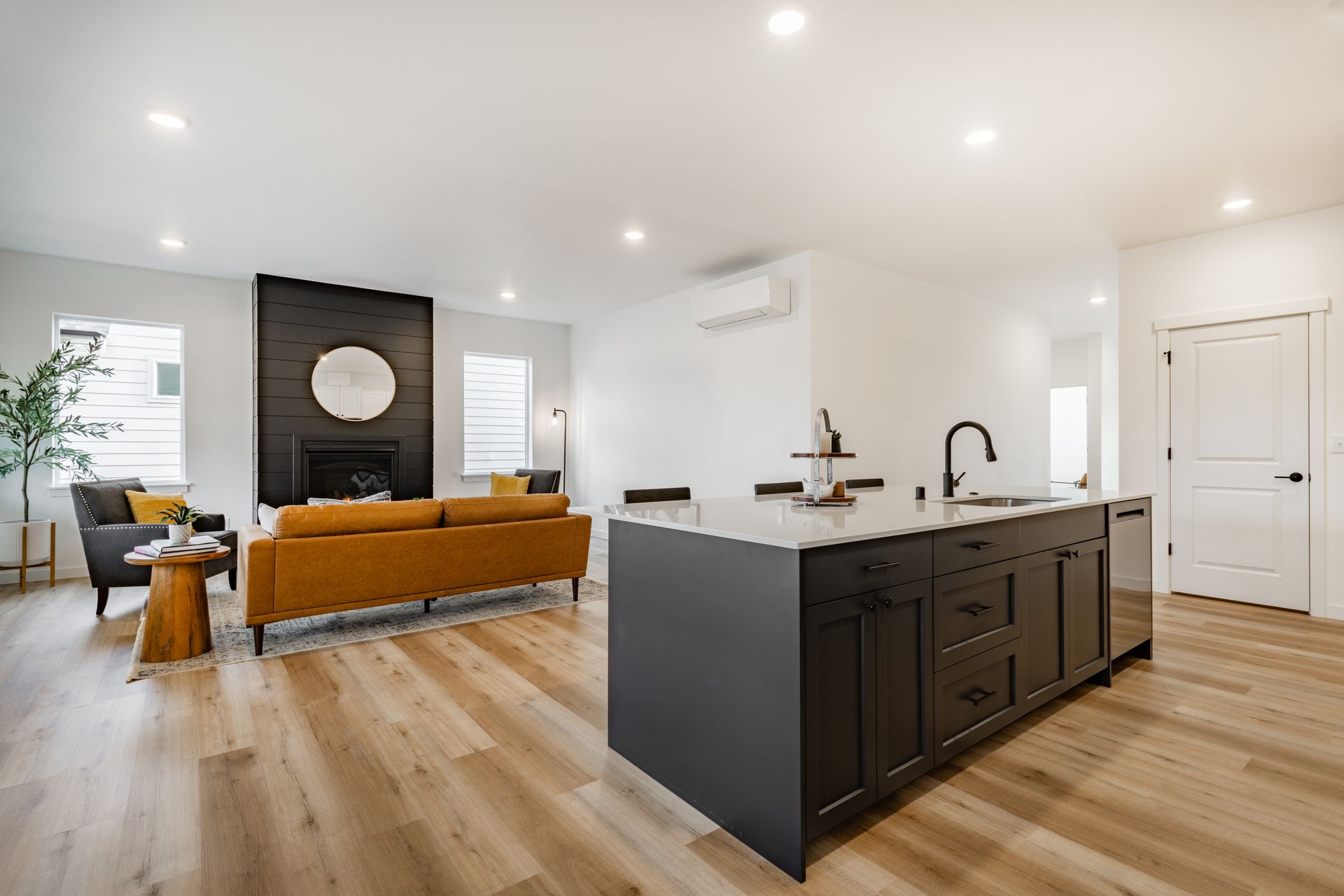 Modern open-concept living room and kitchen with dark island, white cabinets, and tan sofa on wood floors