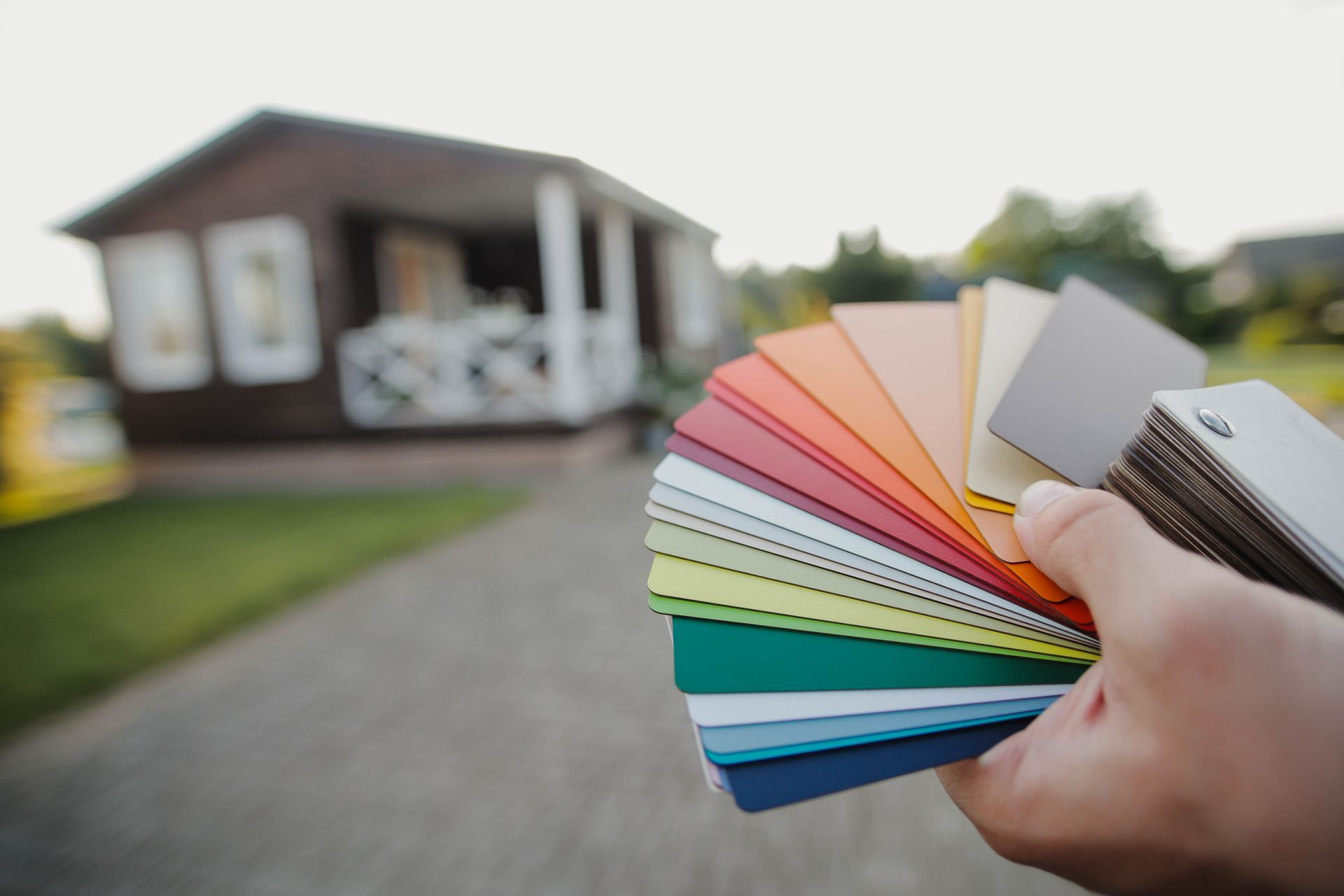 Hand holding a fan of colorful paint swatches in front of a house