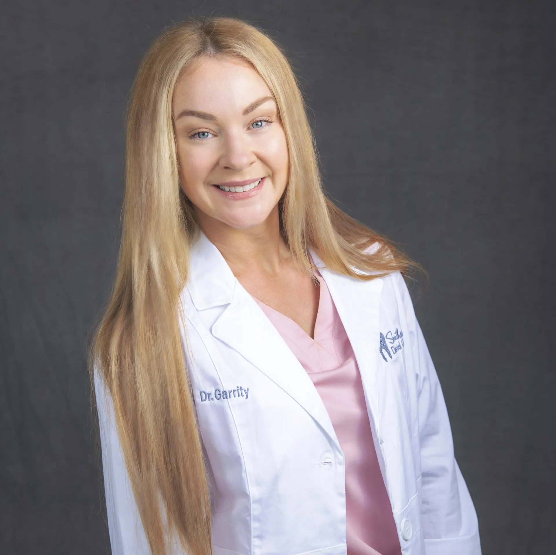 A woman is wearing a white lab coat and smiling.