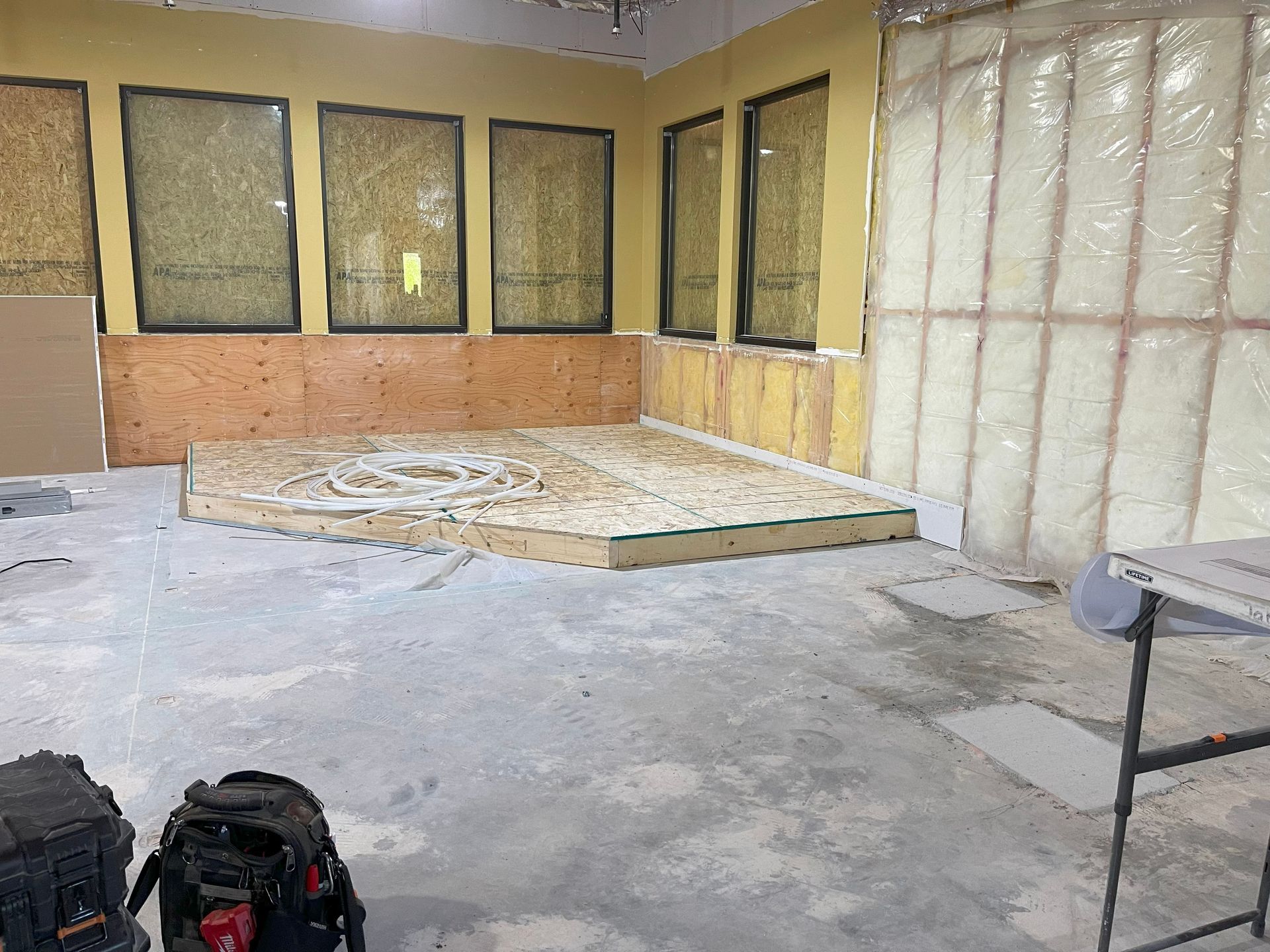 Construction site interior with plywood platform, insulation, and windows.