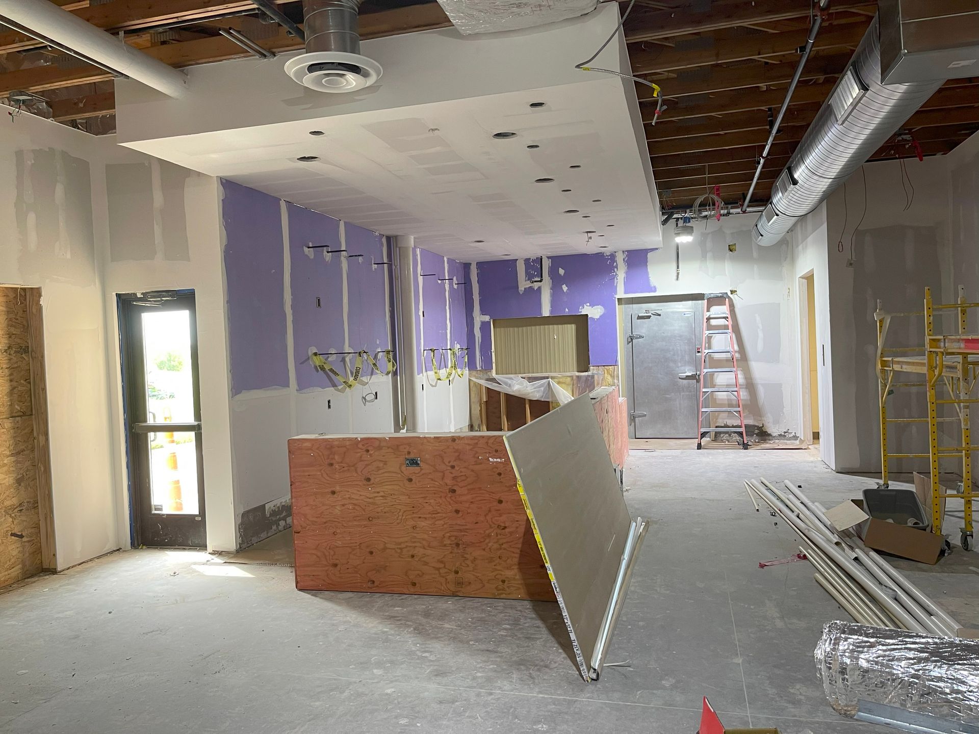 Interior of a building under construction, showing drywall, exposed ceiling, and equipment.