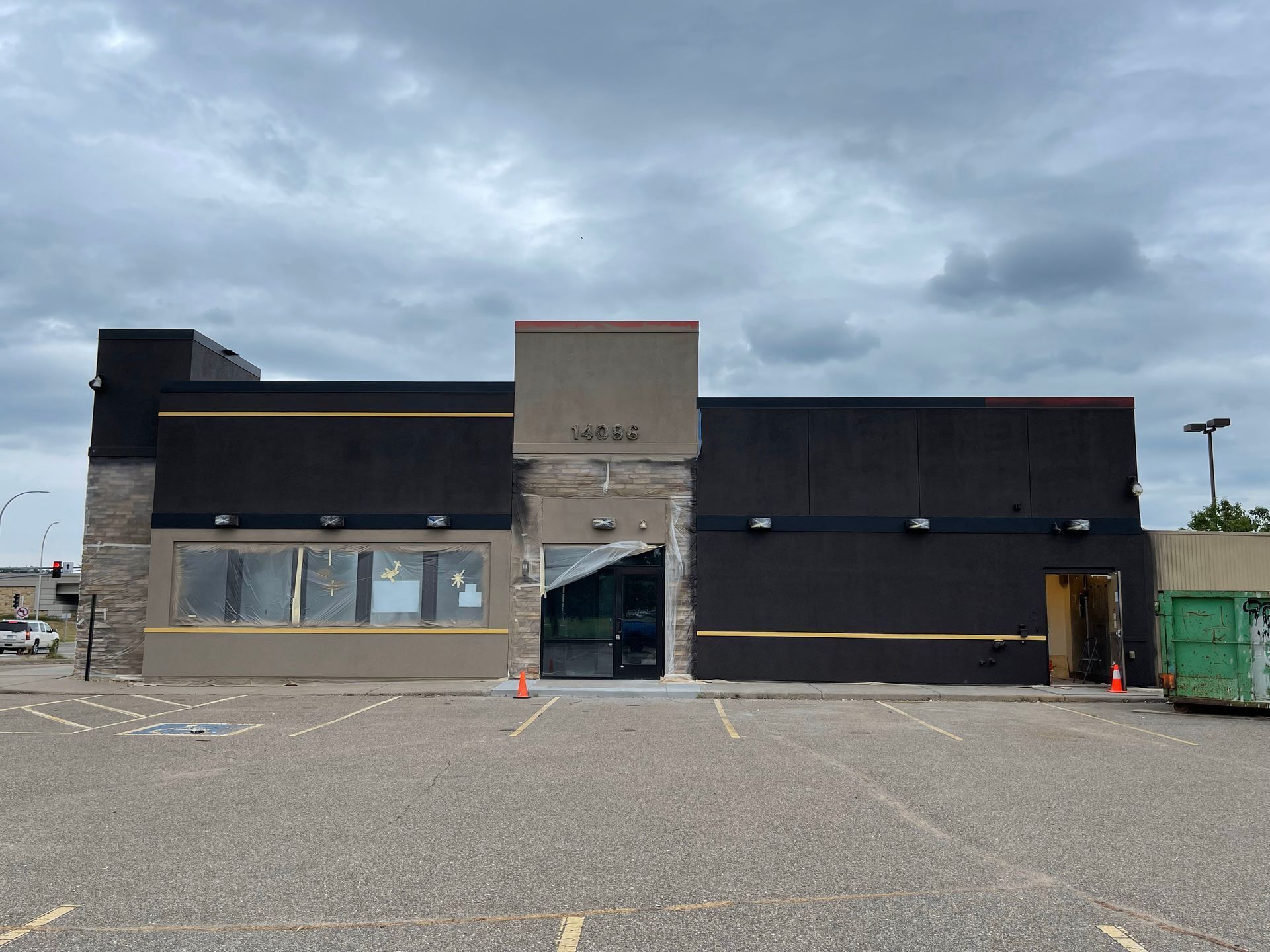 Exterior of a building under renovation, dark walls, beige stone accents, cloudy sky, empty parking lot.