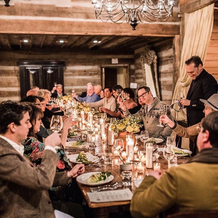 A group of people are sitting at a long table toasting with wine glasses.