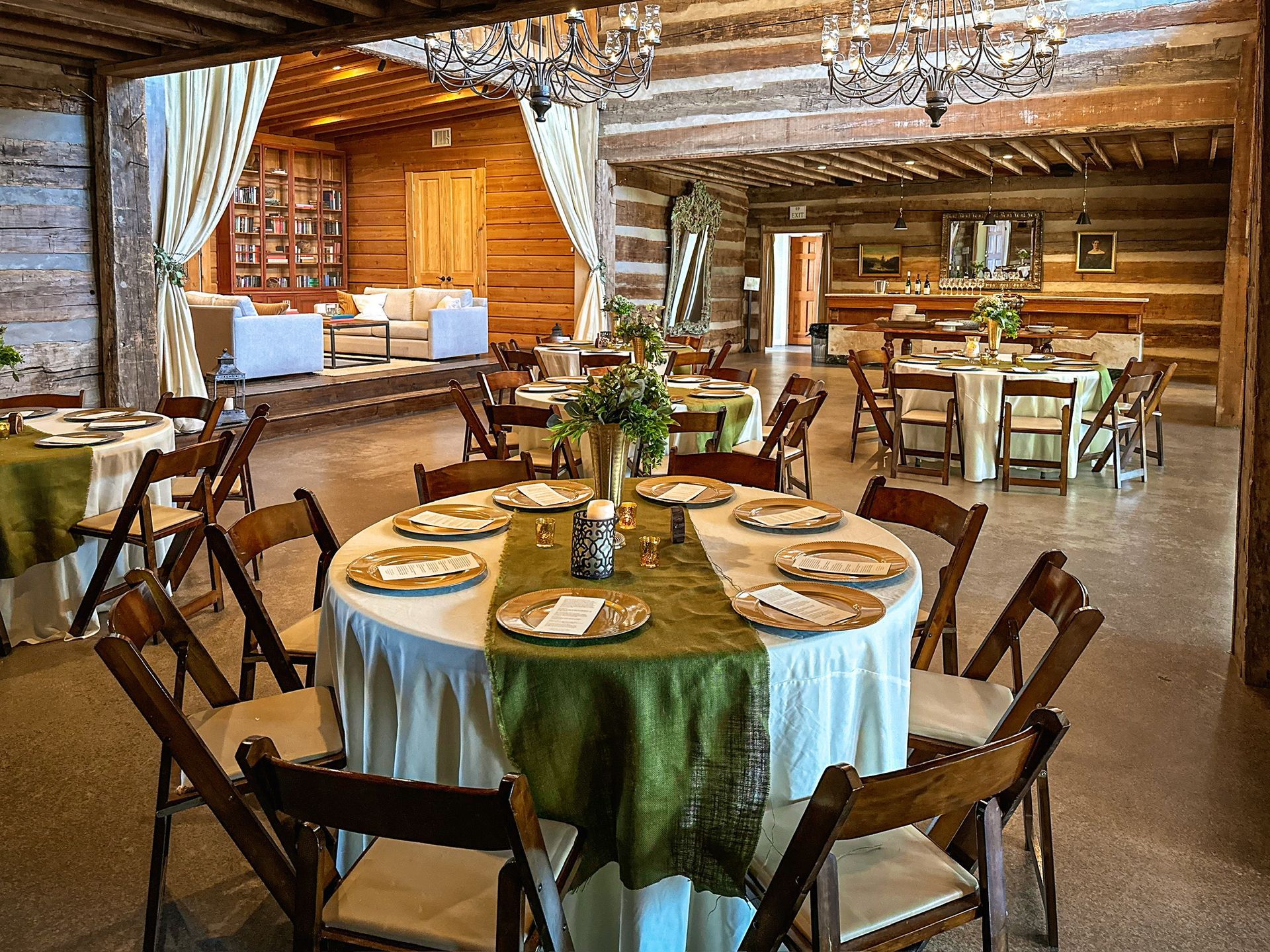Rustic dining room with a round set table, wooden chairs, and a cozy fireplace in the background