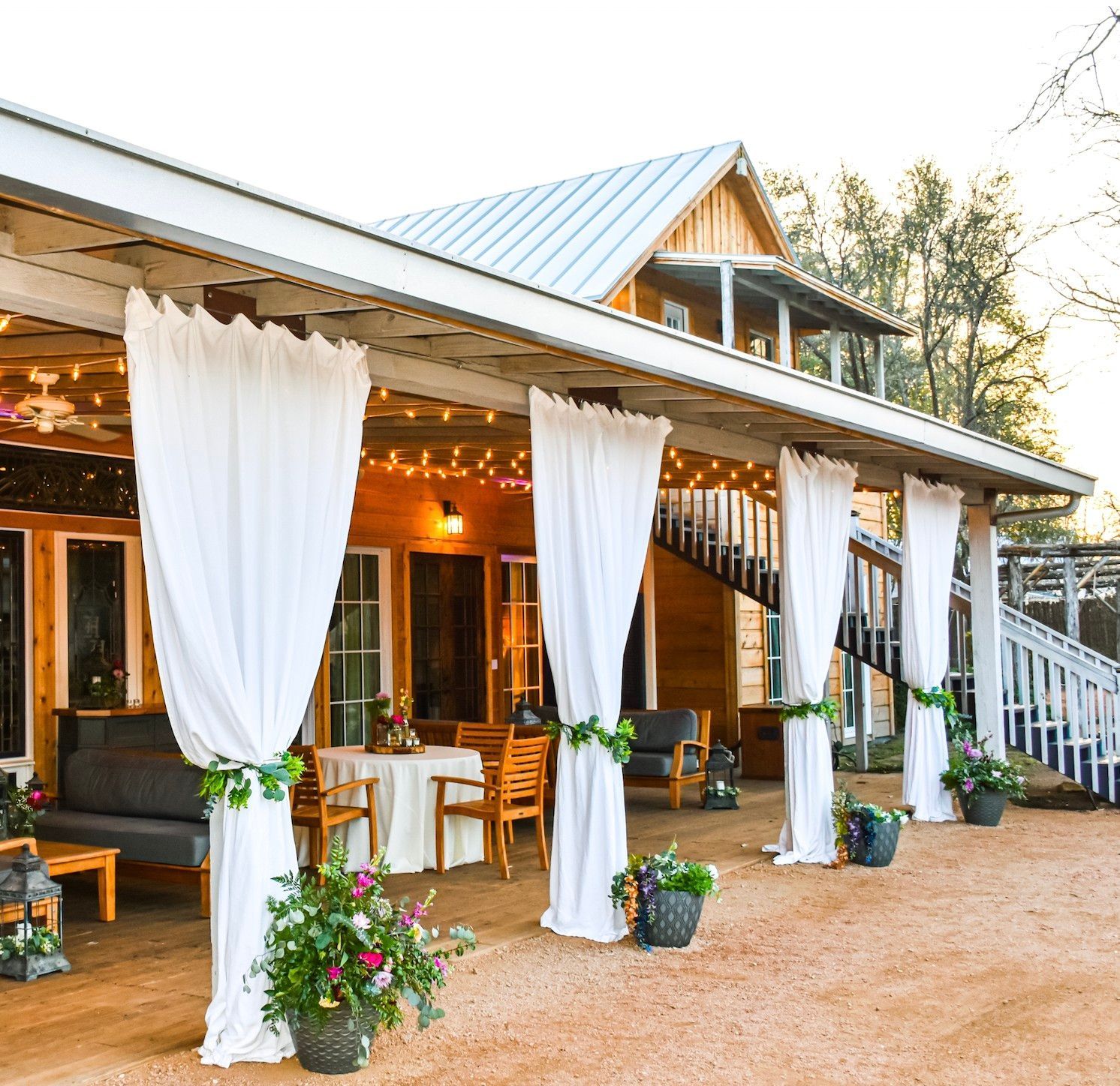 A porch with white curtains and flowers in front of a house