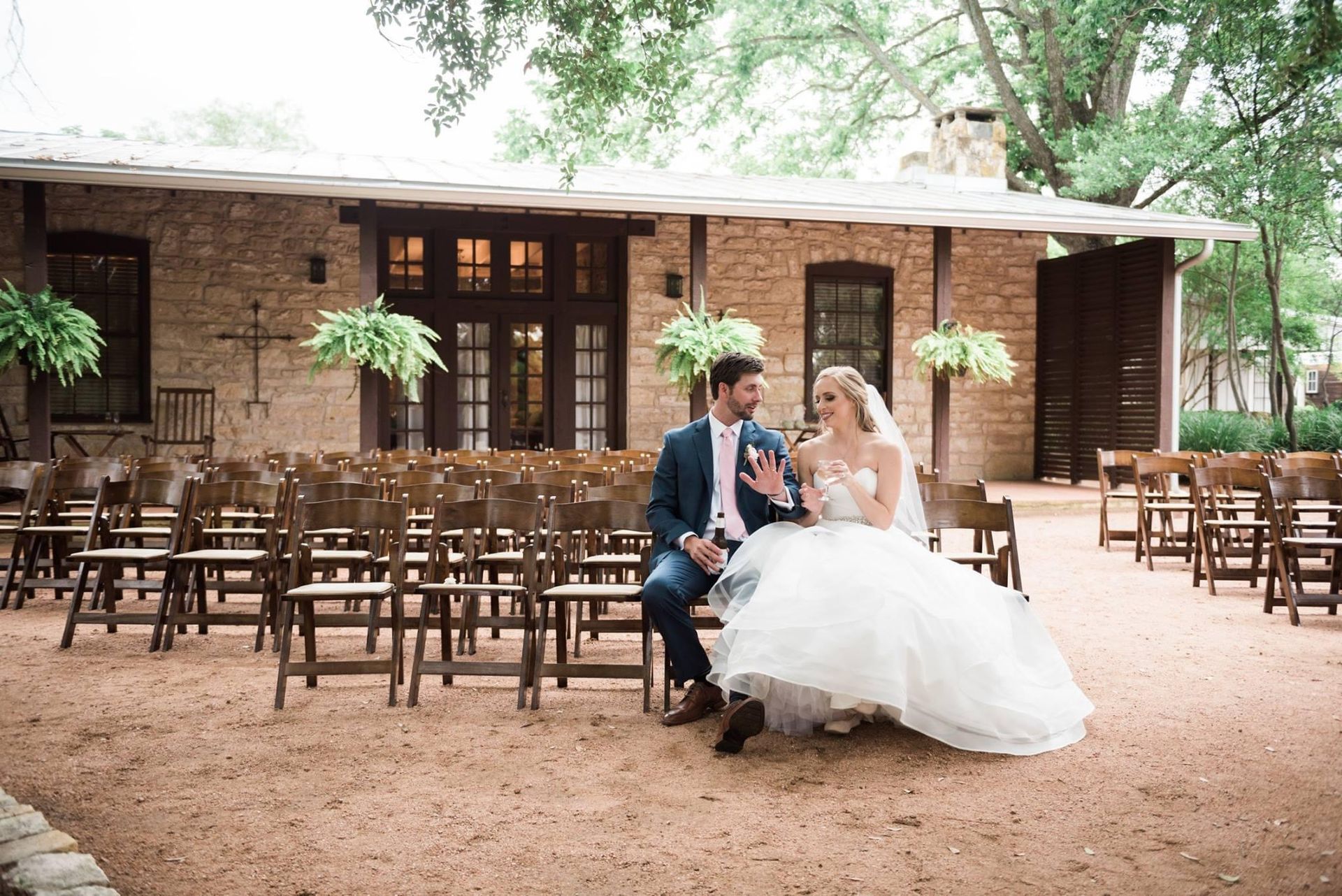 A bride and groom are sitting on a bench in front of a brick building.