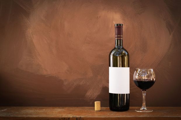 A bottle of wine and a glass of wine are on a wooden table.