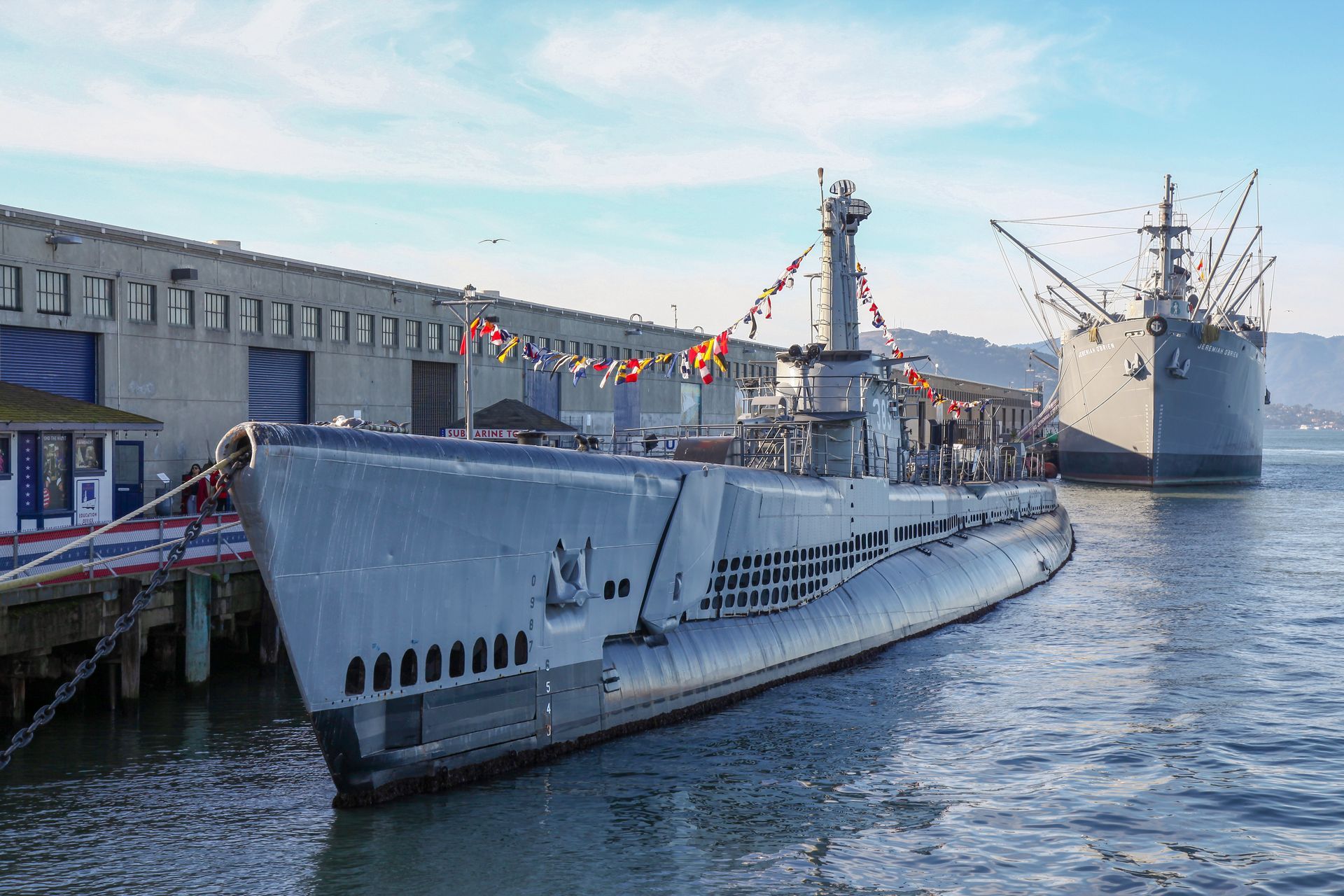 A submarine is docked next to a large ship in the water.