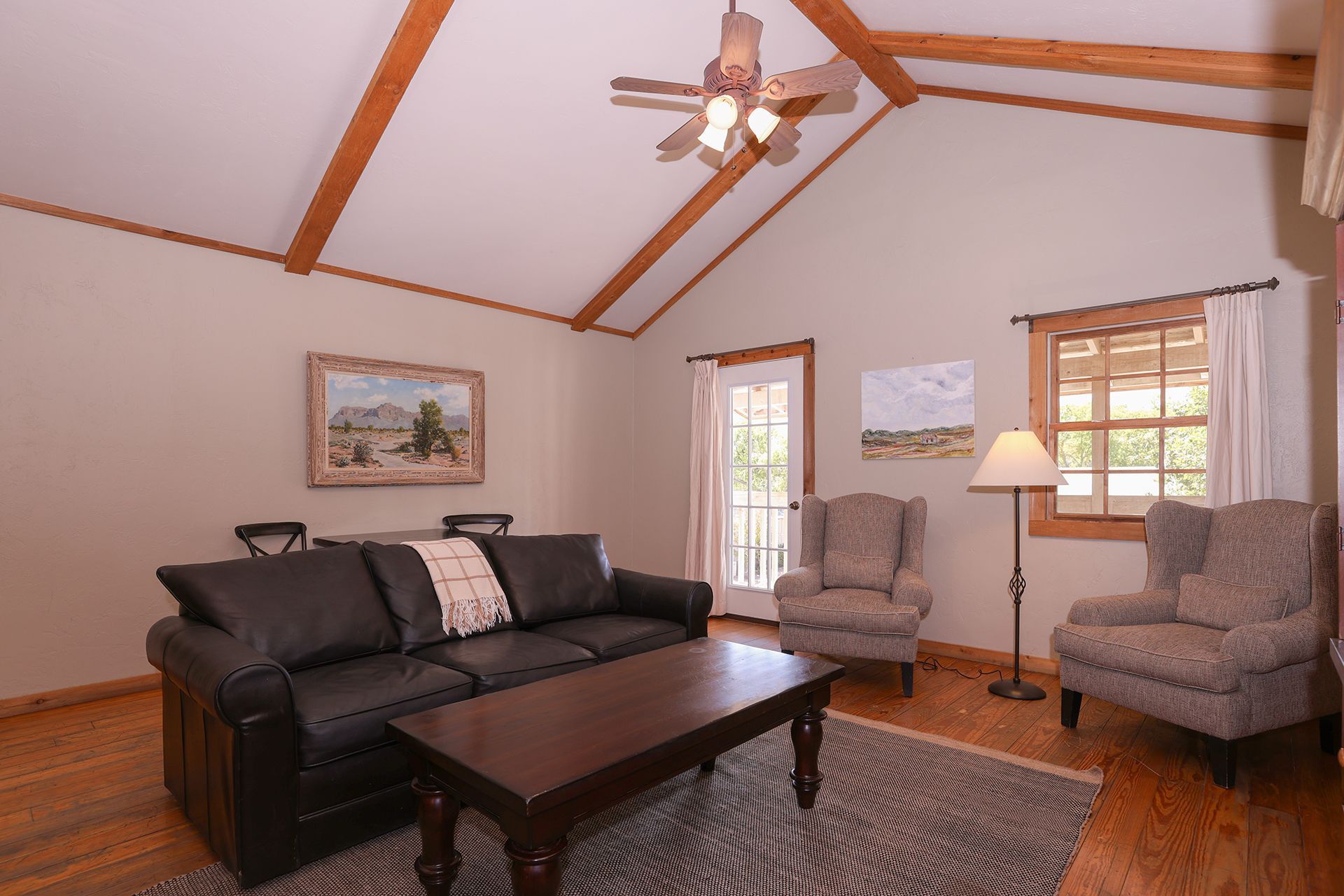 Cozy living room with black sofa, two gray chairs, wooden coffee table, and vaulted ceiling with ceiling fan