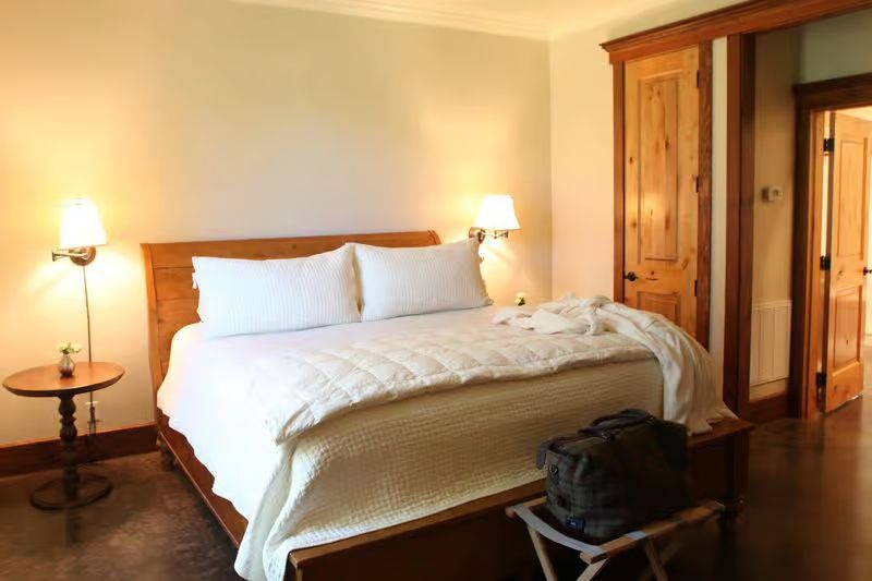A bedroom with a king size bed and a bag on a stool