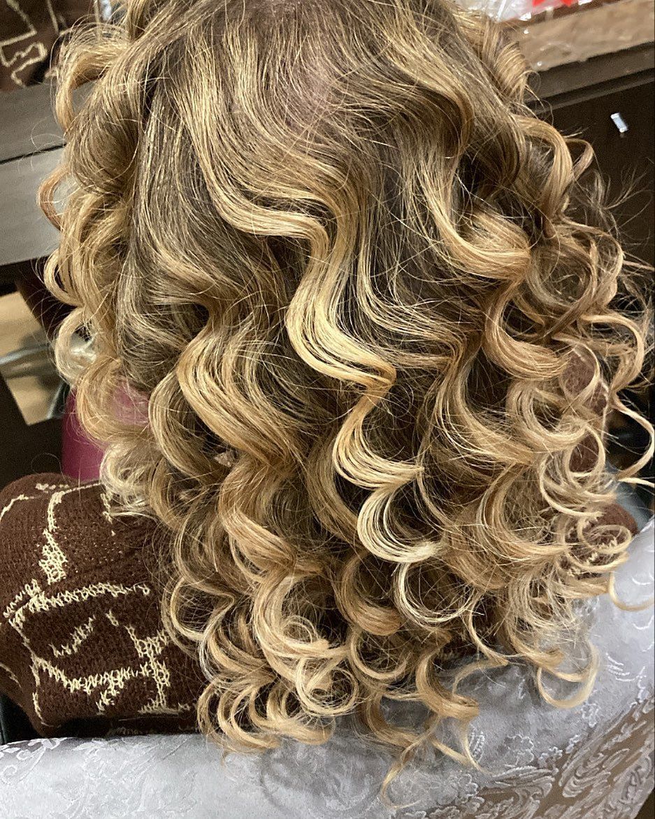 Primo piano di capelli biondi acconciati in riccioli voluminosi e sciolti, visti da dietro.