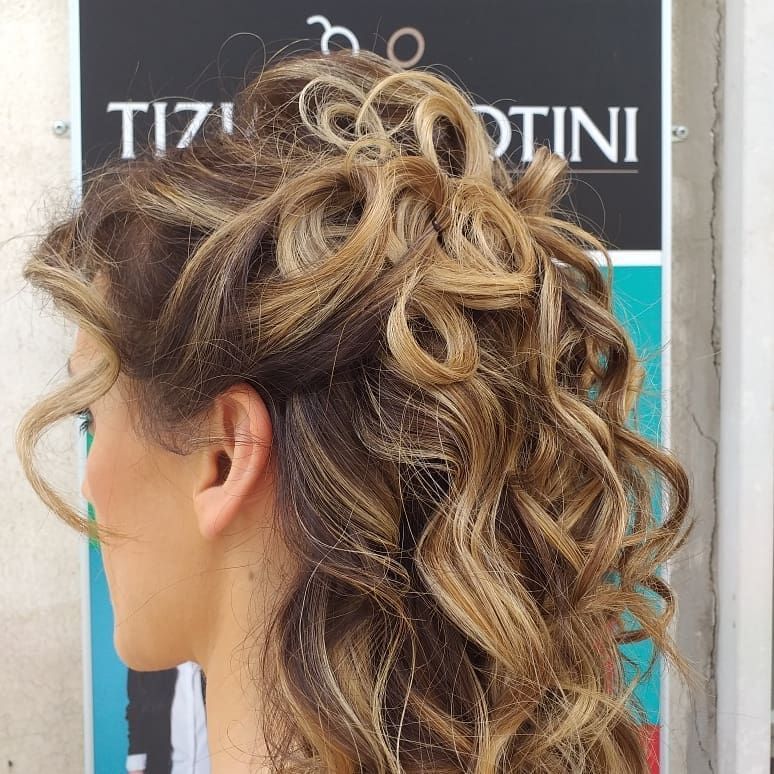 Donna con capelli ricci castano chiaro raccolti, che coprono parzialmente l'orecchio. Cartello sullo sfondo.