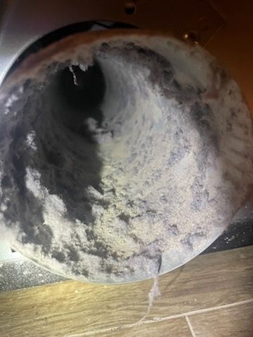 A close-up view inside a dryer vent, heavily clogged with thick, light-colored lint.