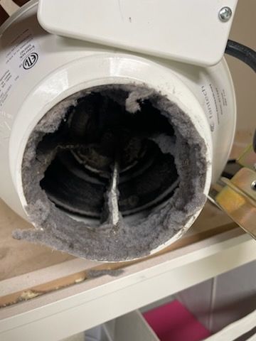 Close-up of a dryer vent clogged with thick gray lint, with a white fan housing visible.