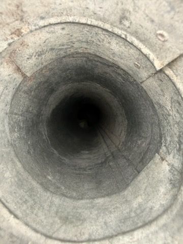 Looking down into a dark, cylindrical hole with concrete or stone rings around the edges.