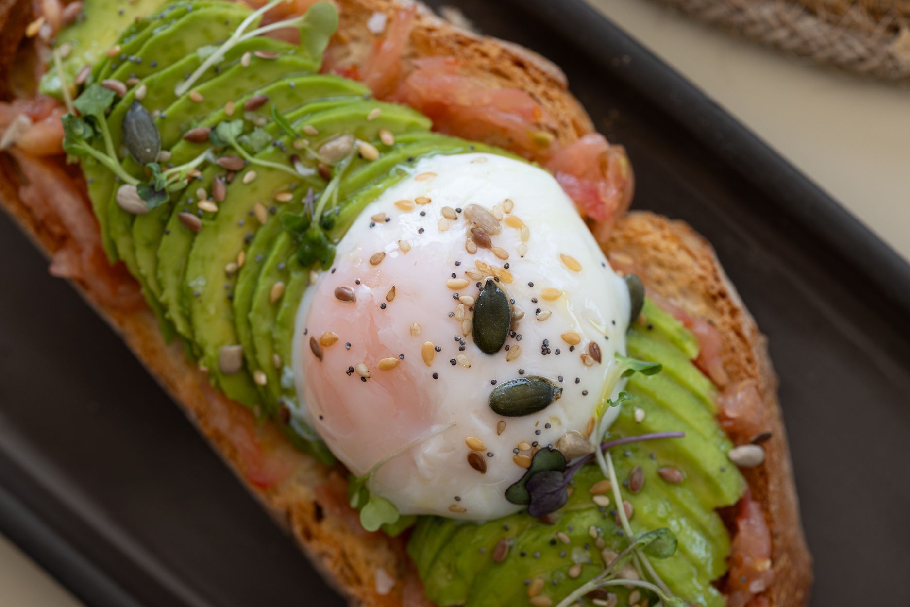 Tostada de aguacate cubierta con un huevo escalfado, hierbas y semillas en un plato.