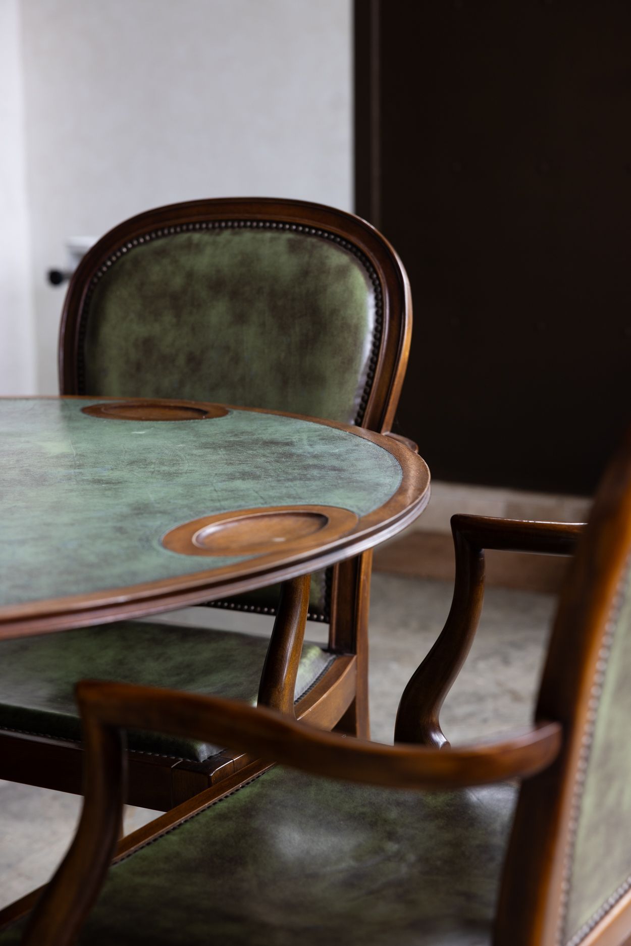 Mesa redonda con sillas de terciopelo verde en un comedor con luz tenue.