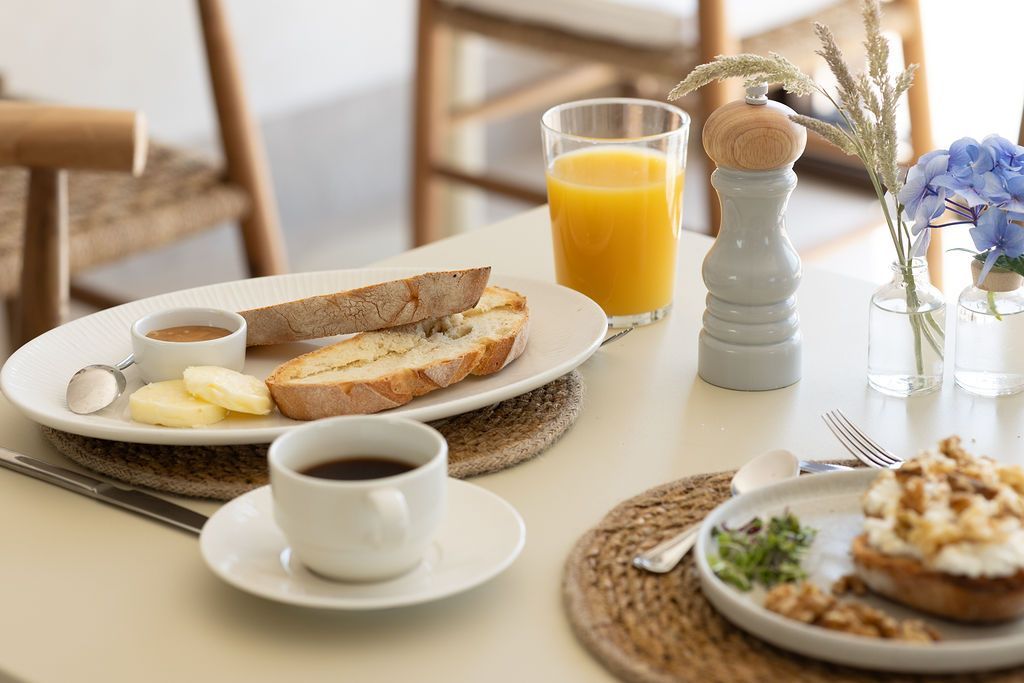 Mesa de desayuno con café, zumo de naranja, tostadas, huevos y bollería en un luminoso comedor.