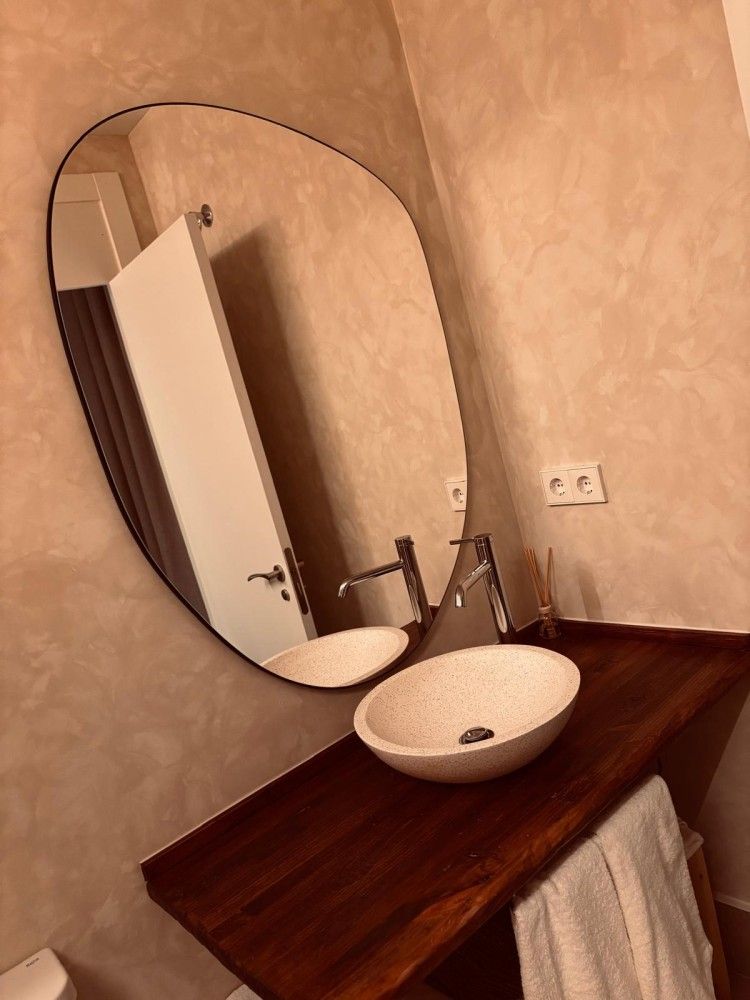 Mueble de baño pequeño con espejo ovalado, lavabo redondo blanco, encimera de madera y toallero debajo.