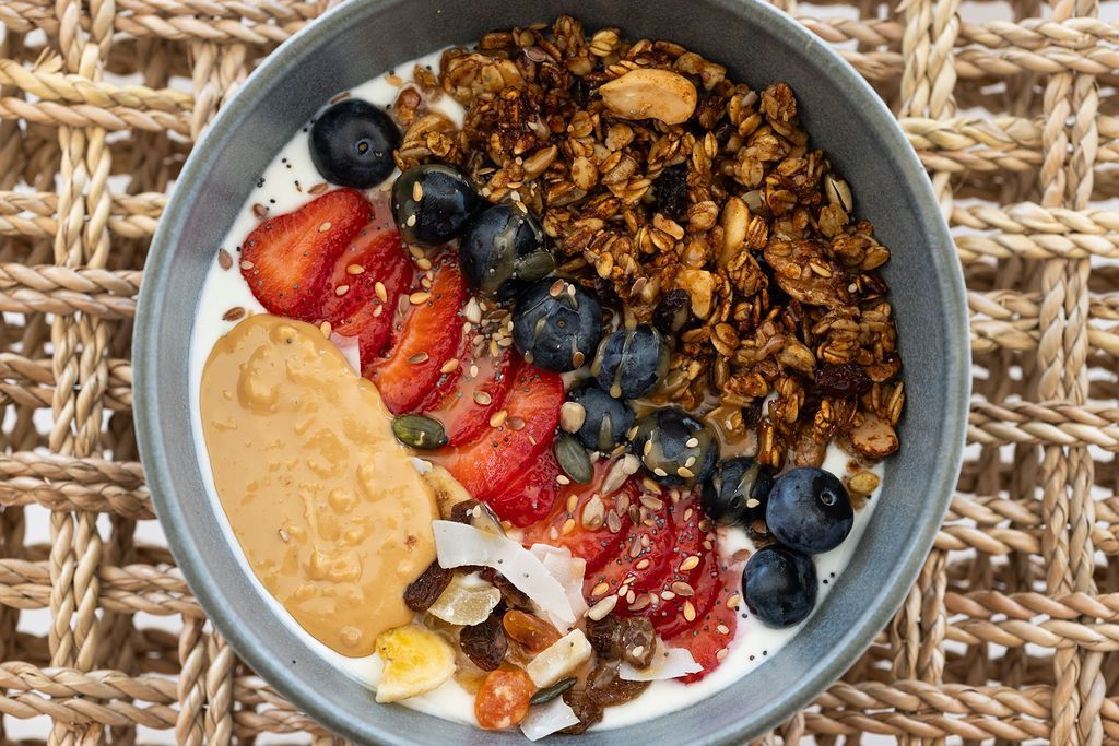 Un bol de granola, fresas, arándanos y mantequilla de cacahuete sobre un mantel individual tejido.