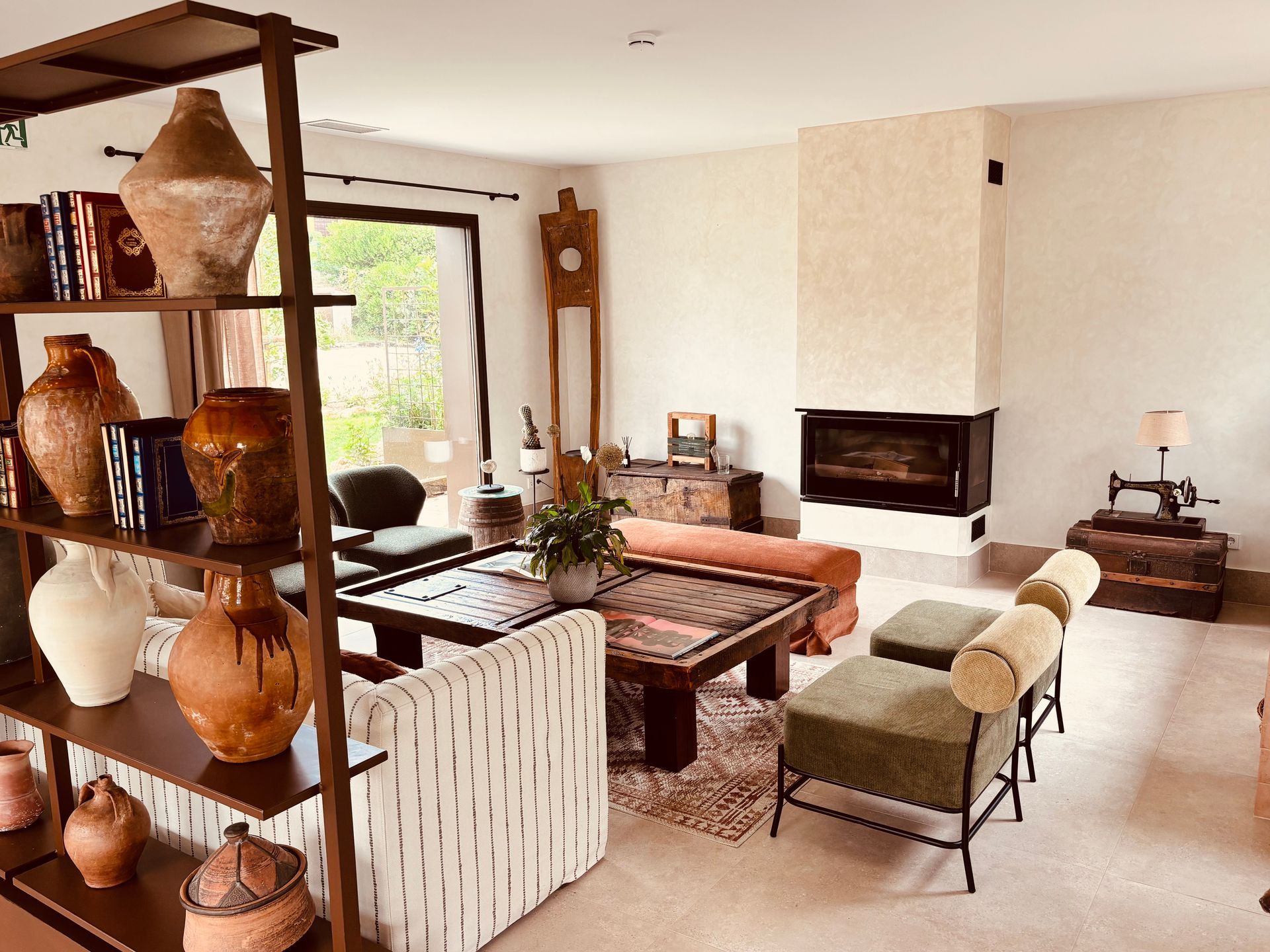 Acogedora sala de estar con chimenea, sofás a rayas, decoración tejida y estanterías con cerámica cerca de una ventana luminosa.