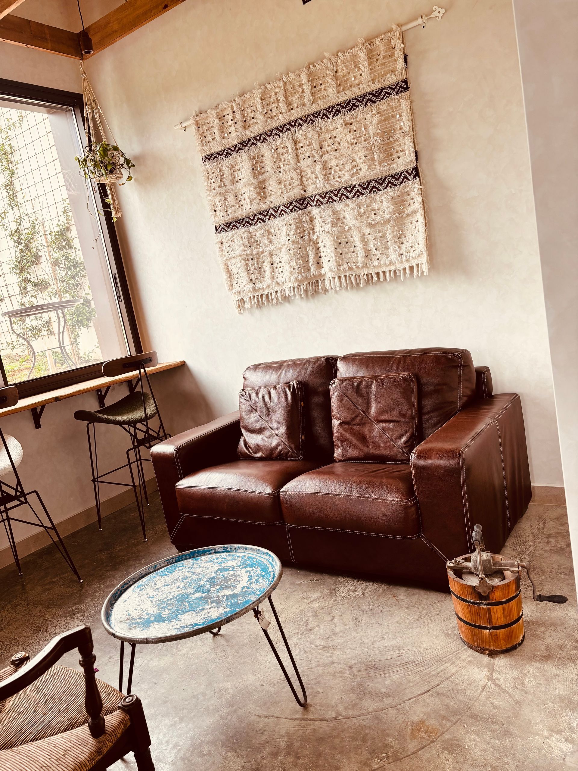 Acogedora sala de estar con sofá de cuero marrón, mesa redonda azul y tapiz tejido junto a la ventana.