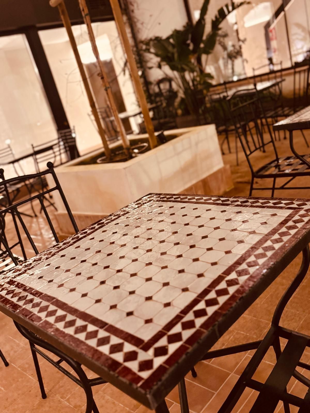 Mesa de café con azulejos y sillas de metal negro en una cálida zona de estar interior.
